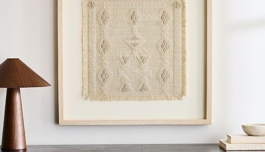 Ingelijst textielwerk met brede passe-partout boven een zwart meubel